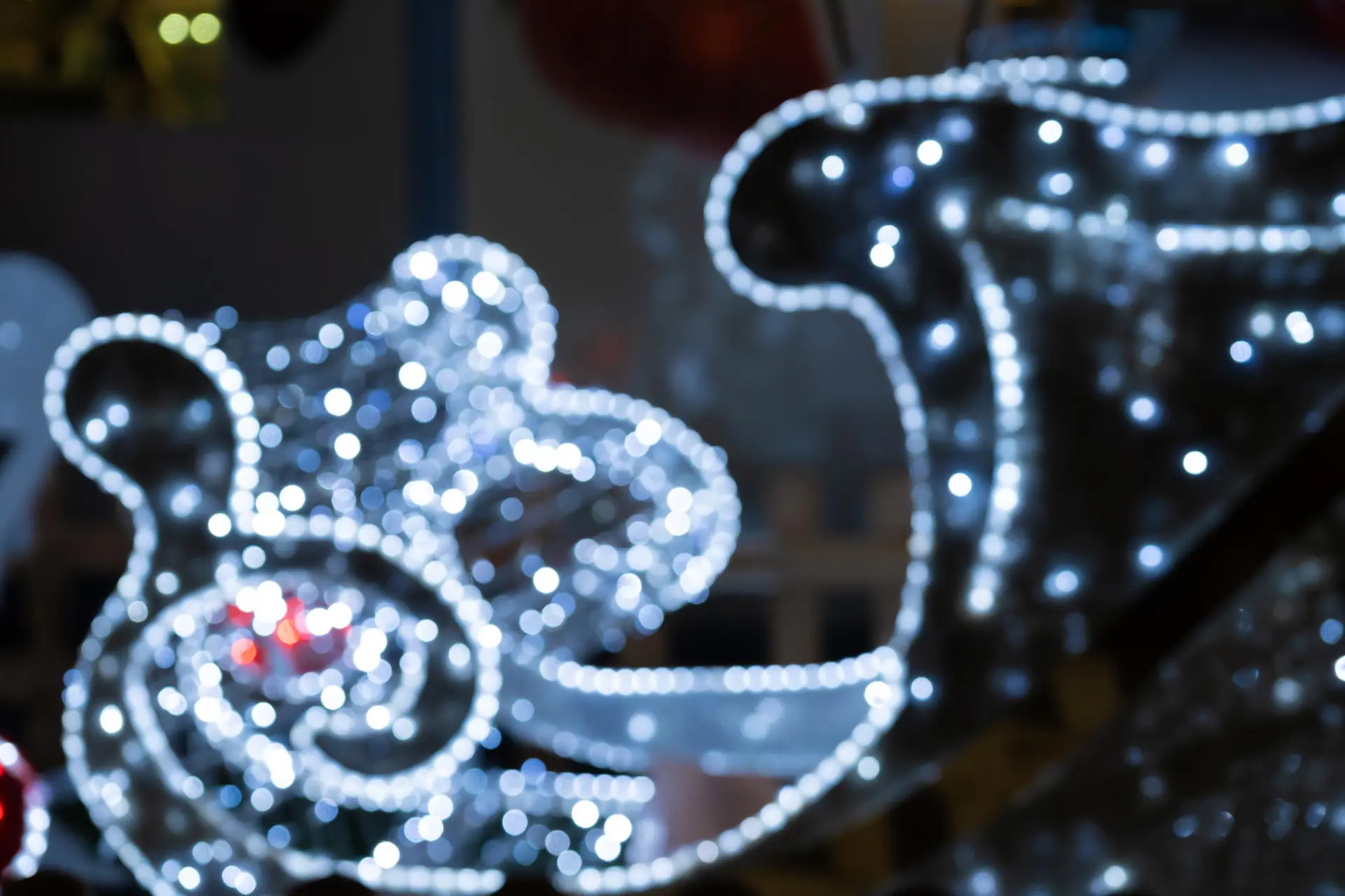 Blurred lights of christmas installation – defocused lights of santa sleigh on night city background. Christmas deer installation in Milan